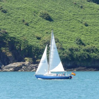 Velero navegando con fondo de calas y montañas de fondo